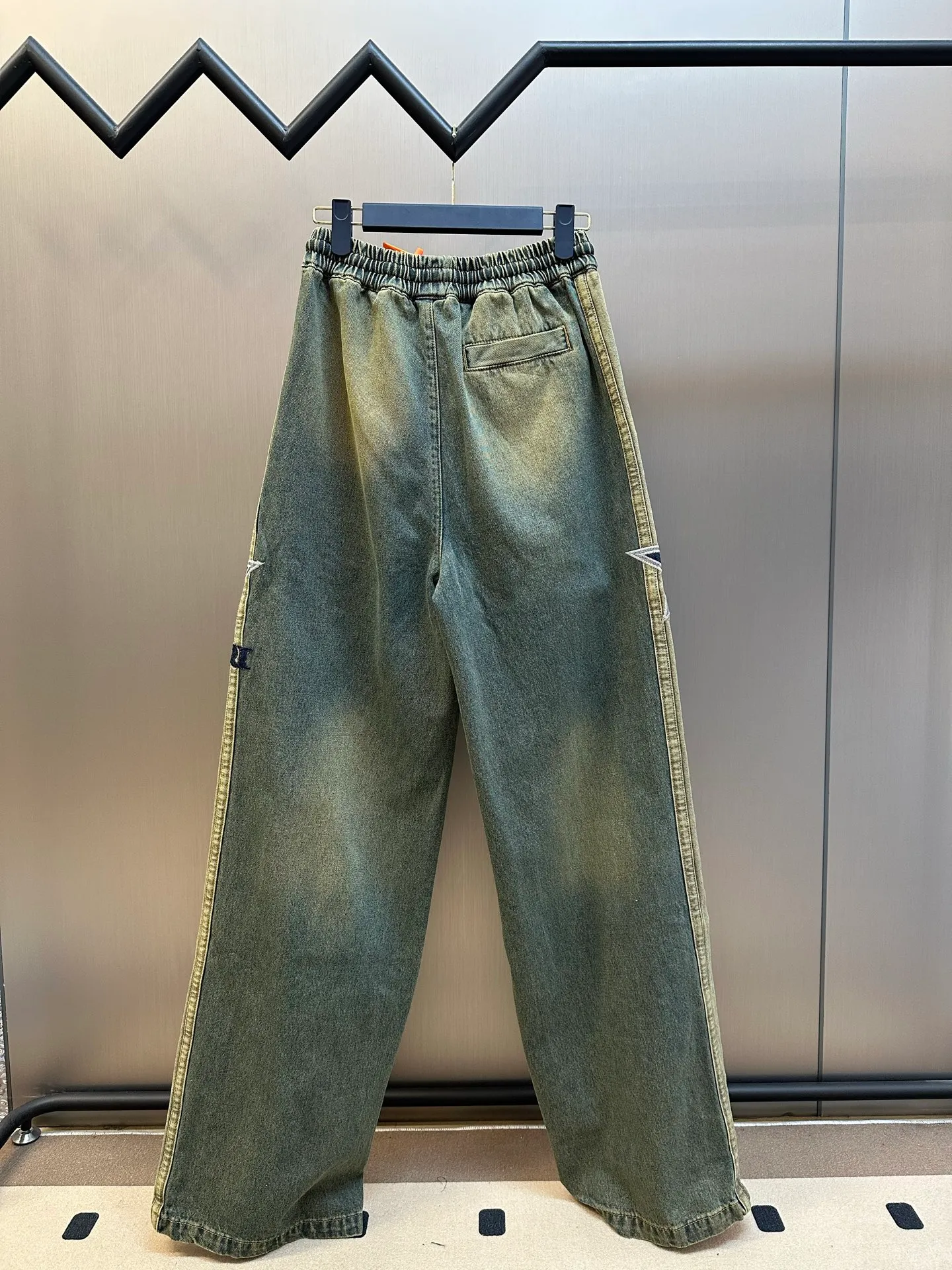 AMIRI logo embroidered jeans, custom-made secret soft high-density denim, charcoal tone moss green washed background, engraved Retro American texture, showing sophisticated and restrained street elegance. The structural tailoring on the side of the trousers is neat and crisp, the high-definition embroidery on both sides is symmetrically laid out, the star emblem totem and the AMIRI letters complement each other, perfectly blending retro accents with high street luxury, and the details are noble and create its own aura. It adopts imported machine embroidery technology, advanced computer control system and precision mechanical components to realize five-pointed star and logo embroidery operations. Priority is given to customizing the 1:1 original denim material, so as to stir-fry snowballs and stir-fry salt. Specially prepare the corresponding solution, add a certain amount of dye, soak the denim material in it to absorb the solvent, then scrub it and dry it to further fade and oxidize it. The whisker rubbing technique is combined with the whisker gun painting technique. Manual rubbing is performed on specific areas first to achieve a natural wrinkle effect, and then specific tools are used to draw the whisker-shaped texture to create a full visual effect. Stone grinding, light fermentation + pulling, bleaching and softening. The mutual friction between the pumice stone and the clothes will cause wear and fading effects on the surface of the denim. Through the combination of pulling and bleaching, the clothes will produce a certain texture and stretching effect while bleaching. size：s m l xl
