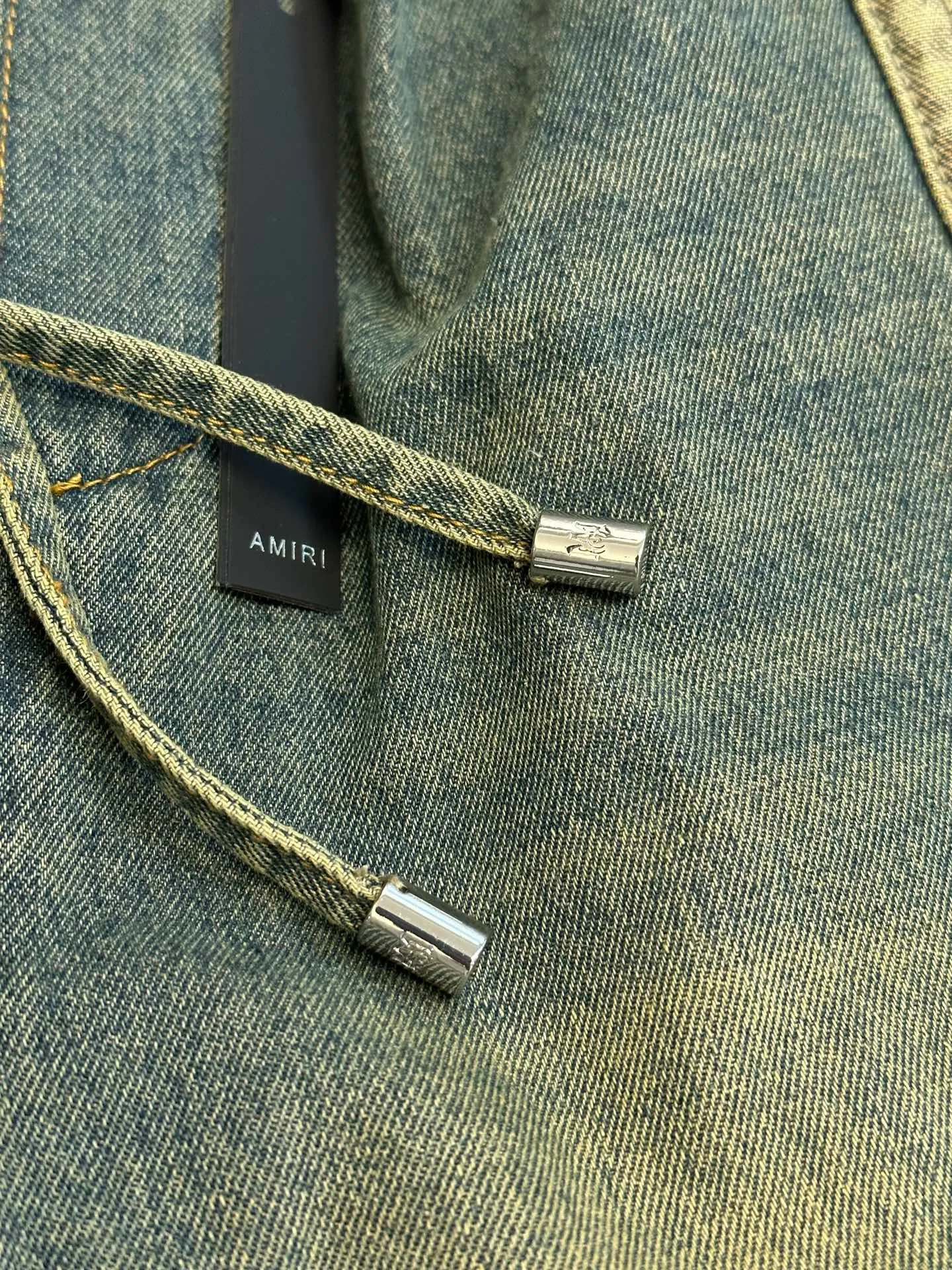 AMIRI logo embroidered jeans, custom-made secret soft high-density denim, charcoal tone moss green washed background, engraved Retro American texture, showing sophisticated and restrained street elegance. The structural tailoring on the side of the trousers is neat and crisp, the high-definition embroidery on both sides is symmetrically laid out, the star emblem totem and the AMIRI letters complement each other, perfectly blending retro accents with high street luxury, and the details are noble and create its own aura. It adopts imported machine embroidery technology, advanced computer control system and precision mechanical components to realize five-pointed star and logo embroidery operations. Priority is given to customizing the 1:1 original denim material, so as to stir-fry snowballs and stir-fry salt. Specially prepare the corresponding solution, add a certain amount of dye, soak the denim material in it to absorb the solvent, then scrub it and dry it to further fade and oxidize it. The whisker rubbing technique is combined with the whisker gun painting technique. Manual rubbing is performed on specific areas first to achieve a natural wrinkle effect, and then specific tools are used to draw the whisker-shaped texture to create a full visual effect. Stone grinding, light fermentation + pulling, bleaching and softening. The mutual friction between the pumice stone and the clothes will cause wear and fading effects on the surface of the denim. Through the combination of pulling and bleaching, the clothes will produce a certain texture and stretching effect while bleaching. size：s m l xl